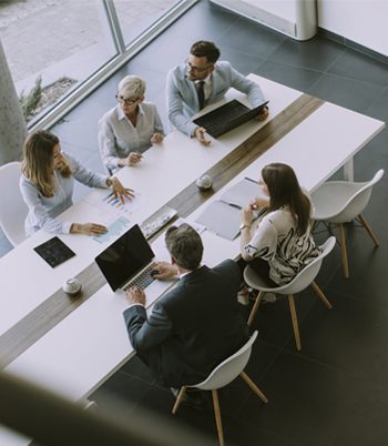 A diverse group of five individuals sitting around a large conference table, engaged in conversation and collaboration