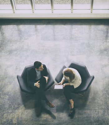 Two individuals seated on chairs in a room having a discussion