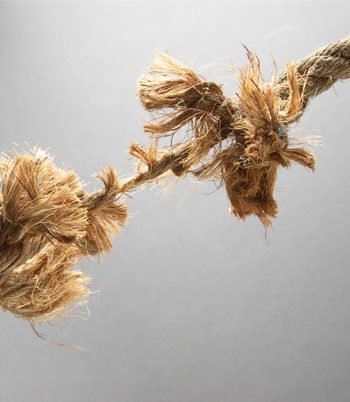 A close up of a frayed rope being pulled against a gray background