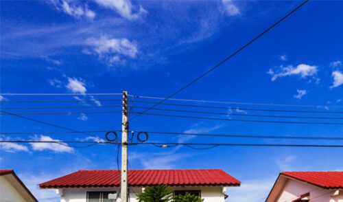 Powerlines in front of a traditional red and white house with a red roof, set against a clear blue sky